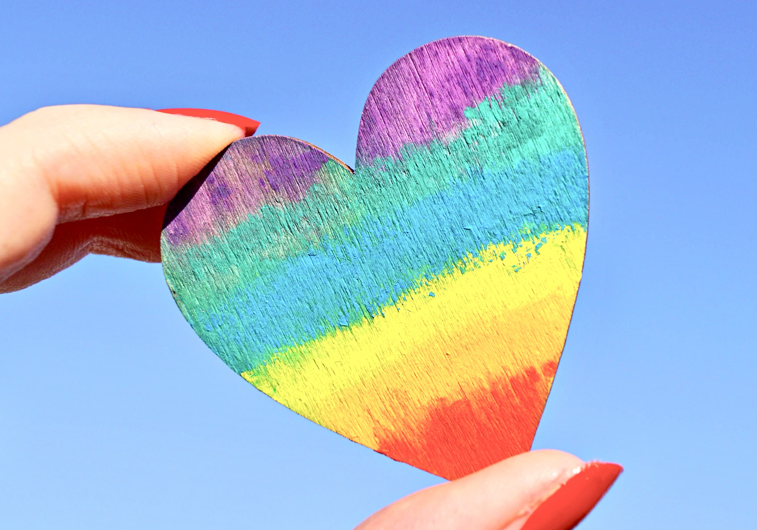 Een regenbooghart tussen twee vingers in de lucht gehouden